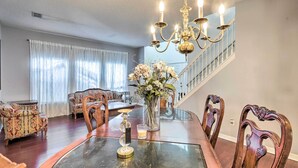 A dining area with a glass table, wooden chairs, a chandelier, and a staircase in the background. - Orlando Home w/ Private Yard + Patio! (Orlando)