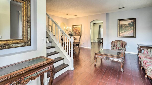 A spacious living room with hardwood flooring, a staircase with white railings, a dining area with a chandelier, and a large mirror on the wall. - Orlando Home w/ Private Yard + Patio! (Orlando)