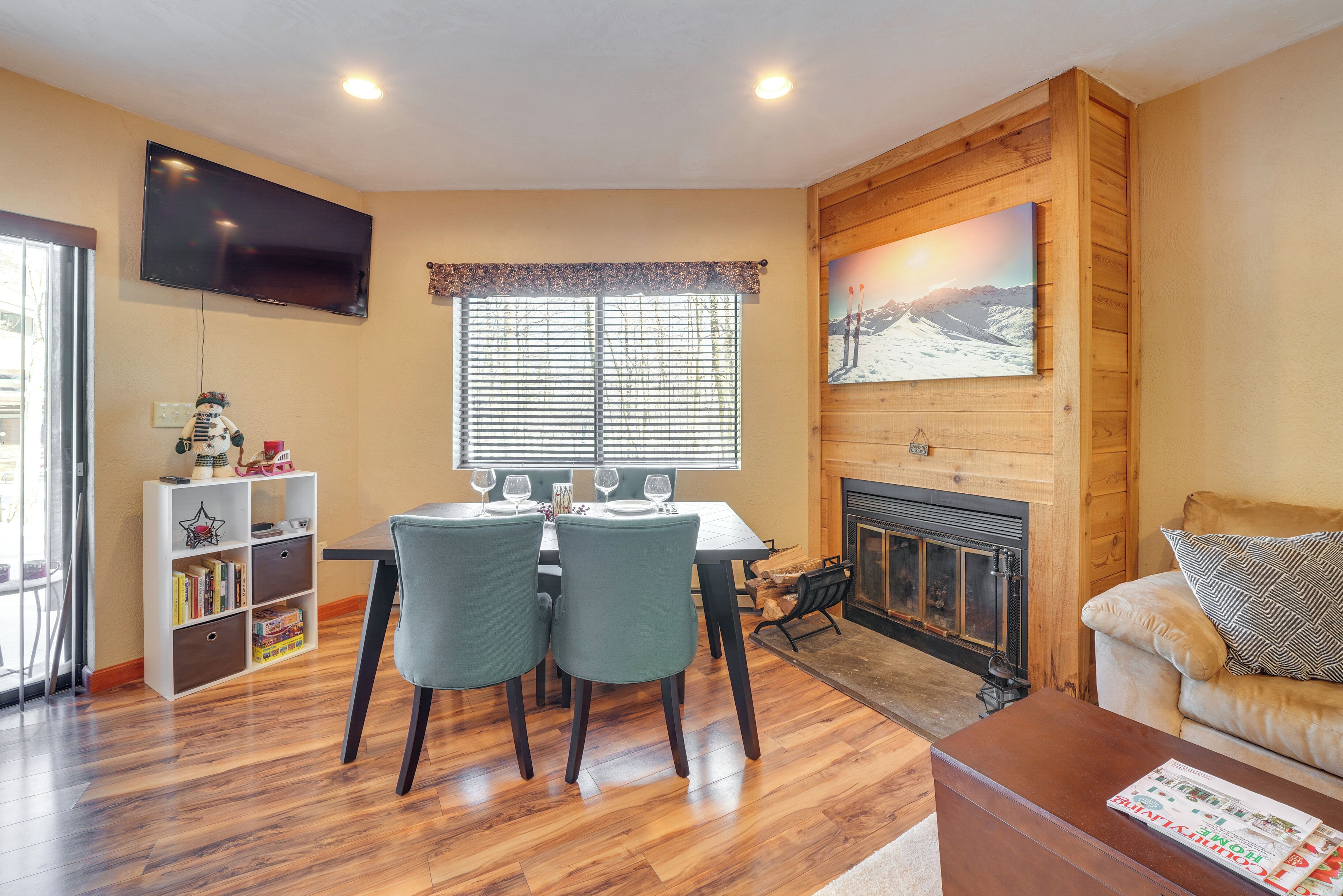 A living room with a fireplace, a television mounted on the wall, and a dining area with chairs and a table.