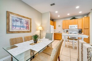 A dining area with a glass table and wicker chairs, a kitchen with wooden cabinets, and a framed picture on the wall. - 6 Mi to Disney: Resort Home w/ Pool Access! (Kissimmee)