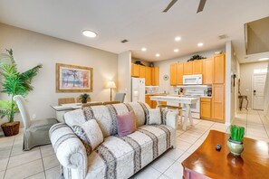 A living room with a sofa, a dining table, and a kitchen area with wooden cabinets and appliances. - 6 Mi to Disney: Resort Home w/ Pool Access! (Kissimmee)