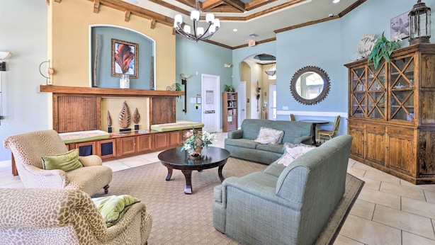 A spacious living room with a high ceiling, wooden beams, and a chandelier. There are two sofas, a coffee table, and a cabinet with decorative items. - 6 Mi to Disney: Resort Home w/ Pool Access! (Kissimmee)