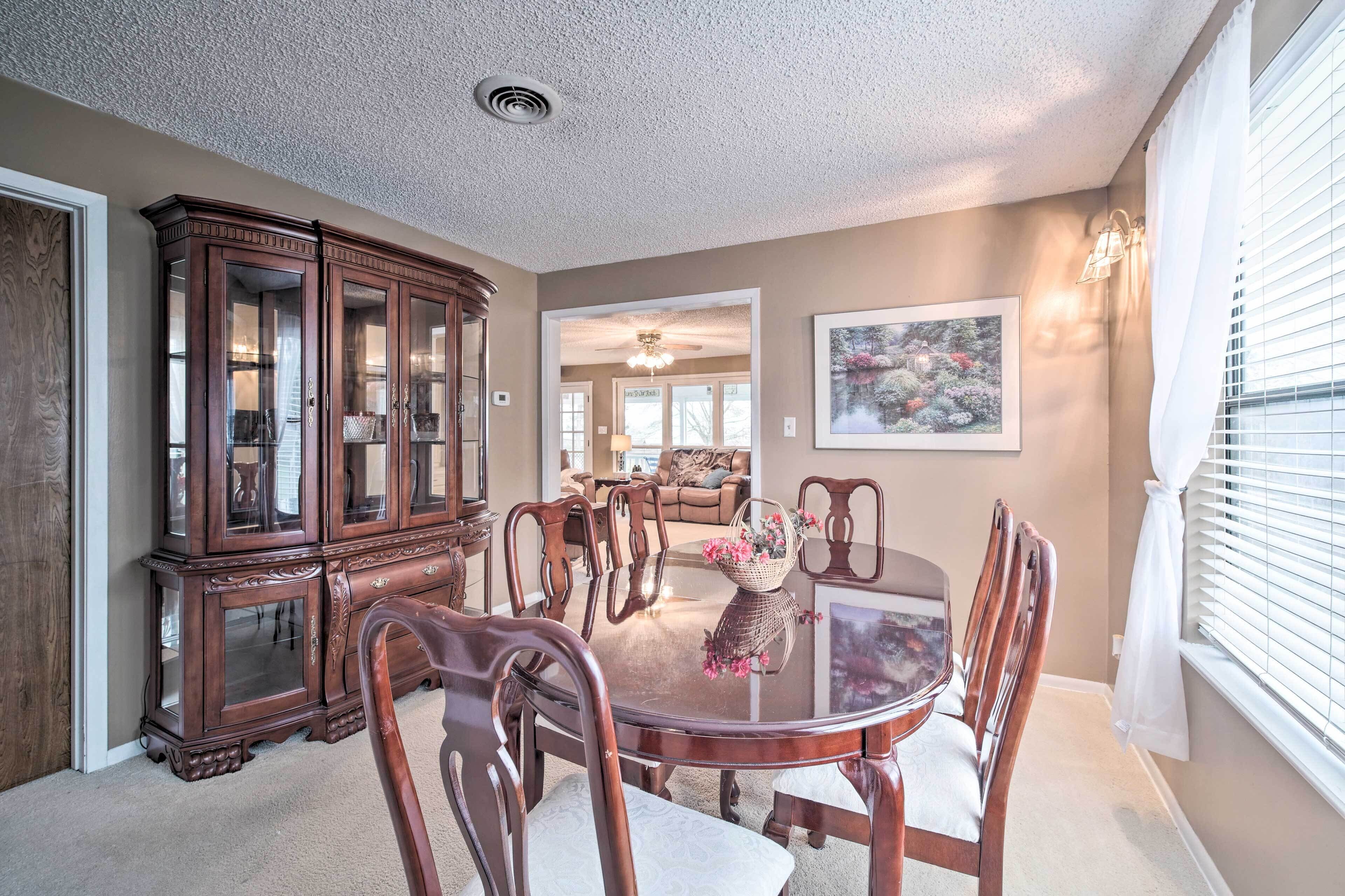 A dining room with a round table, wooden chairs, a dark wooden cabinet, and a painting on the wall.