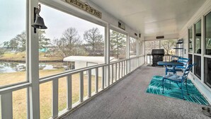 Eine überdachte Veranda mit einem Schild, das 'Willkommen auf unserer Veranda' sagt, einer Klingel und Blick auf einen See und Häuser.