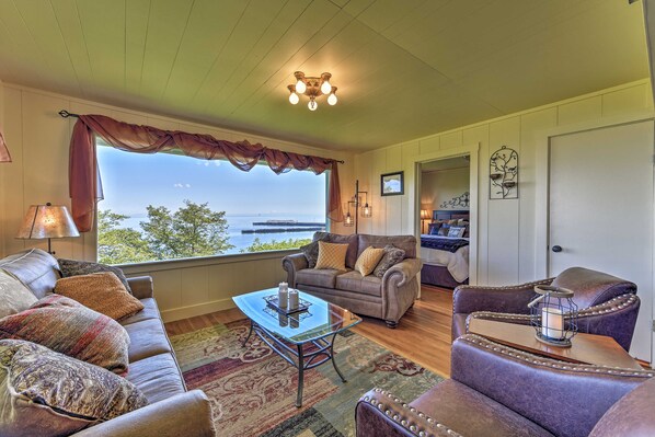 A cozy living room with a large window, a leather sofa, a glass coffee table, and a view of the outdoors.