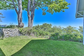 A backyard with a stone wall, two large trees, and a well-maintained lawn. - Waterfront Home ~ 6 Mi to Olympic National Park! (Port Angeles)