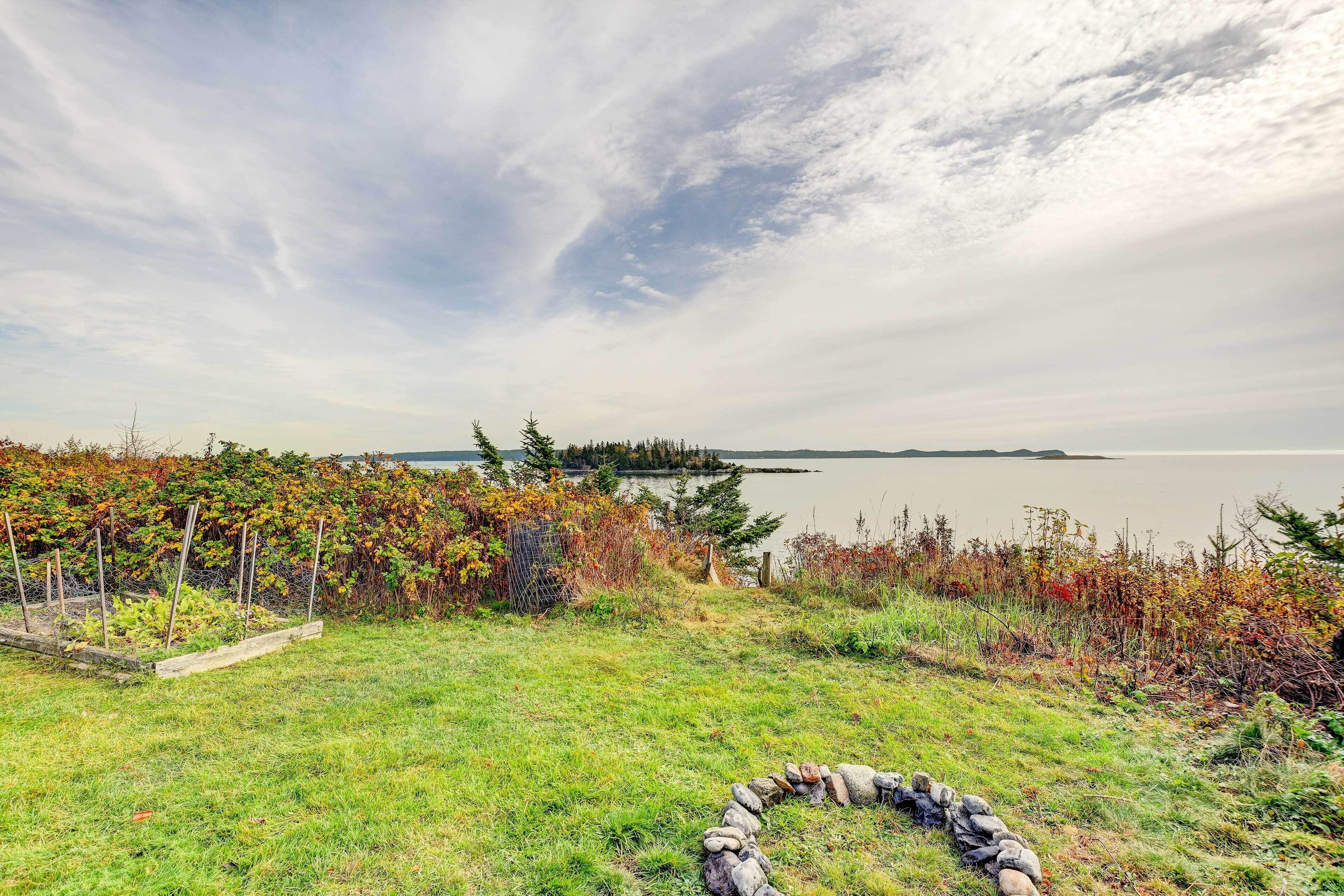 A grassy area with a stone wall and a view of a lake and forest.