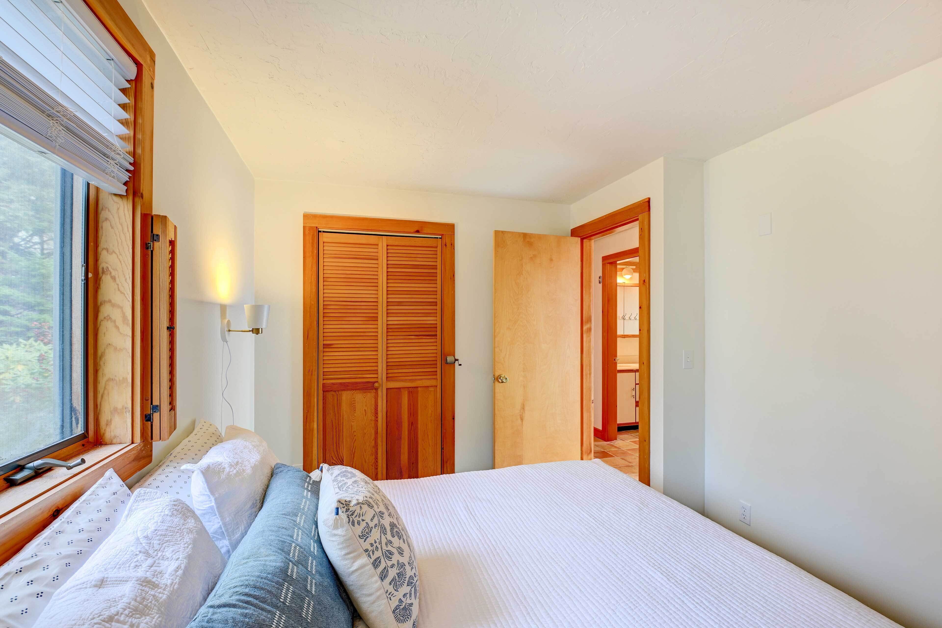 A bedroom with a bed, two bedside tables, a window with blinds, and a wooden door.