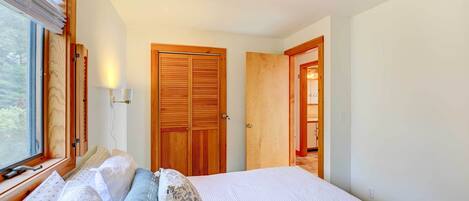 A bedroom with a bed, two bedside tables, a window with blinds, and a wooden door.