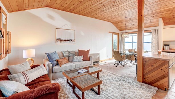 A cozy living room with a wooden ceiling, a sofa set, a coffee table, and a view of the kitchen and dining area. - Serene Jonesport Escape: Deck w/ Water Views! (Jonesport)