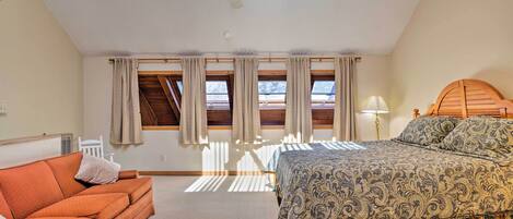 Un dormitorio con cama, sofá, ventilador de techo y ventanas amplias con cortinas.