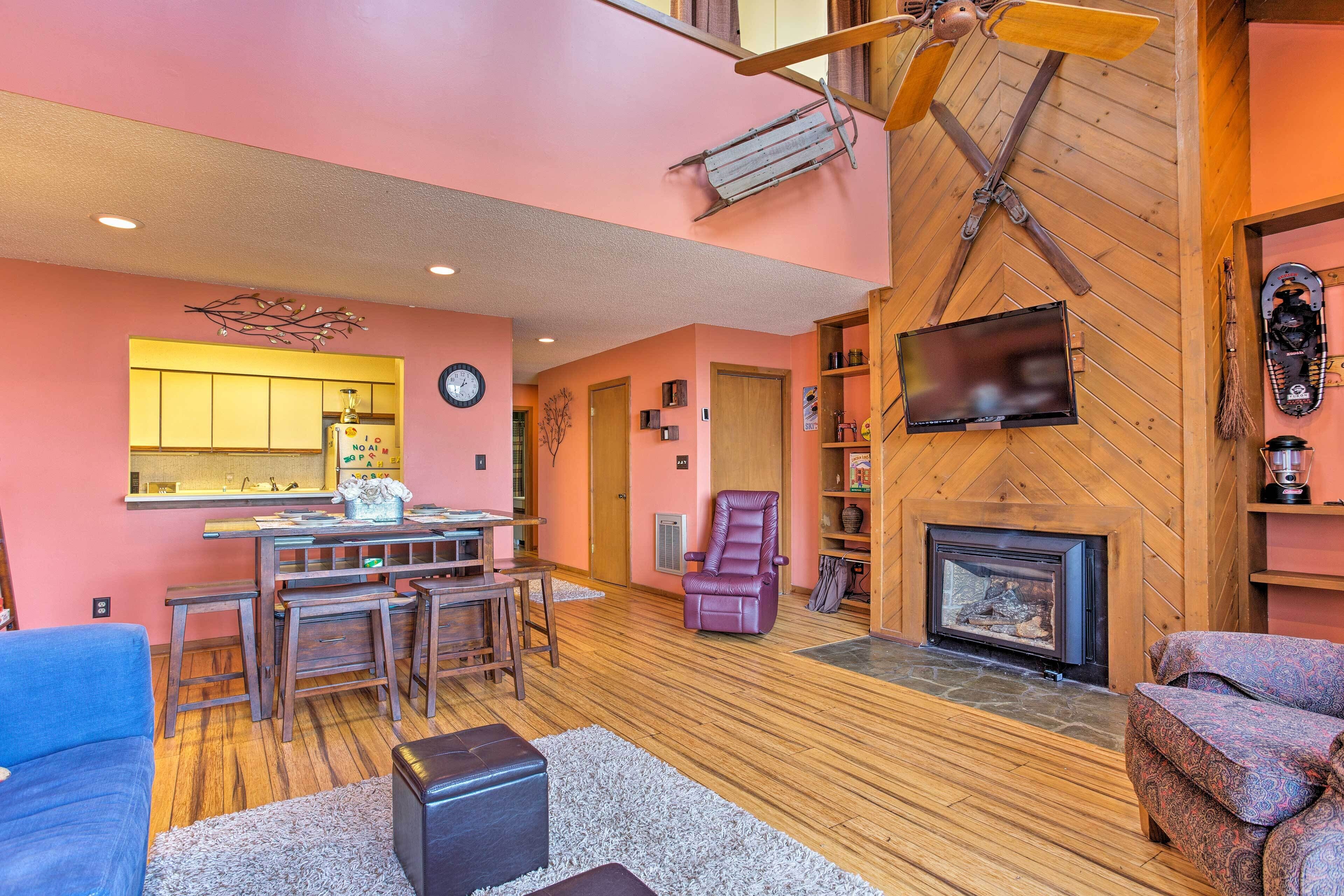 Un salon chaleureux avec une cheminée, un plancher en bois et un coin repas doté d’un bar.