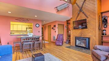 Un salon chaleureux avec une cheminée, un plancher en bois et un coin repas doté d’un bar.