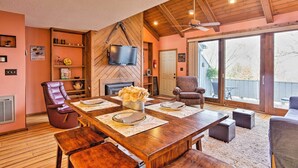 Un vaste salon comprenant une table à manger en bois pour quatre personnes, une cheminée, un téléviseur fixé au mur et une grande porte-fenêtre coulissante donnant sur un espace extérieur.