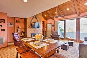 Un salón espacioso con una mesa de comedor de madera dispuesta para cuatro personas, una chimenea, un televisor montado en la pared y un gran ventanal corredero que da a un área exterior.