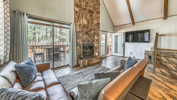 A spacious living room with a stone fireplace, leather sofas, and a large sliding glass door leading to an outdoor patio.