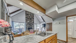 A kitchen with granite countertops, wooden cabinets, a stone accent wall, and a large window overlooking a deck.