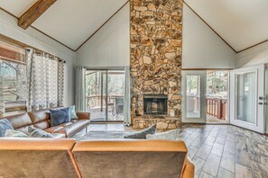 A spacious living room with a stone fireplace, leather sofa, and large windows. - Ruidoso Family Cabin, Short Walk to Downtown! (Ruidoso)
