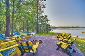 A deck with Adirondack chairs, a fire pit, and a lake view. - Bright Minong Vacation Rental on Little Sand Lake! (Minong)