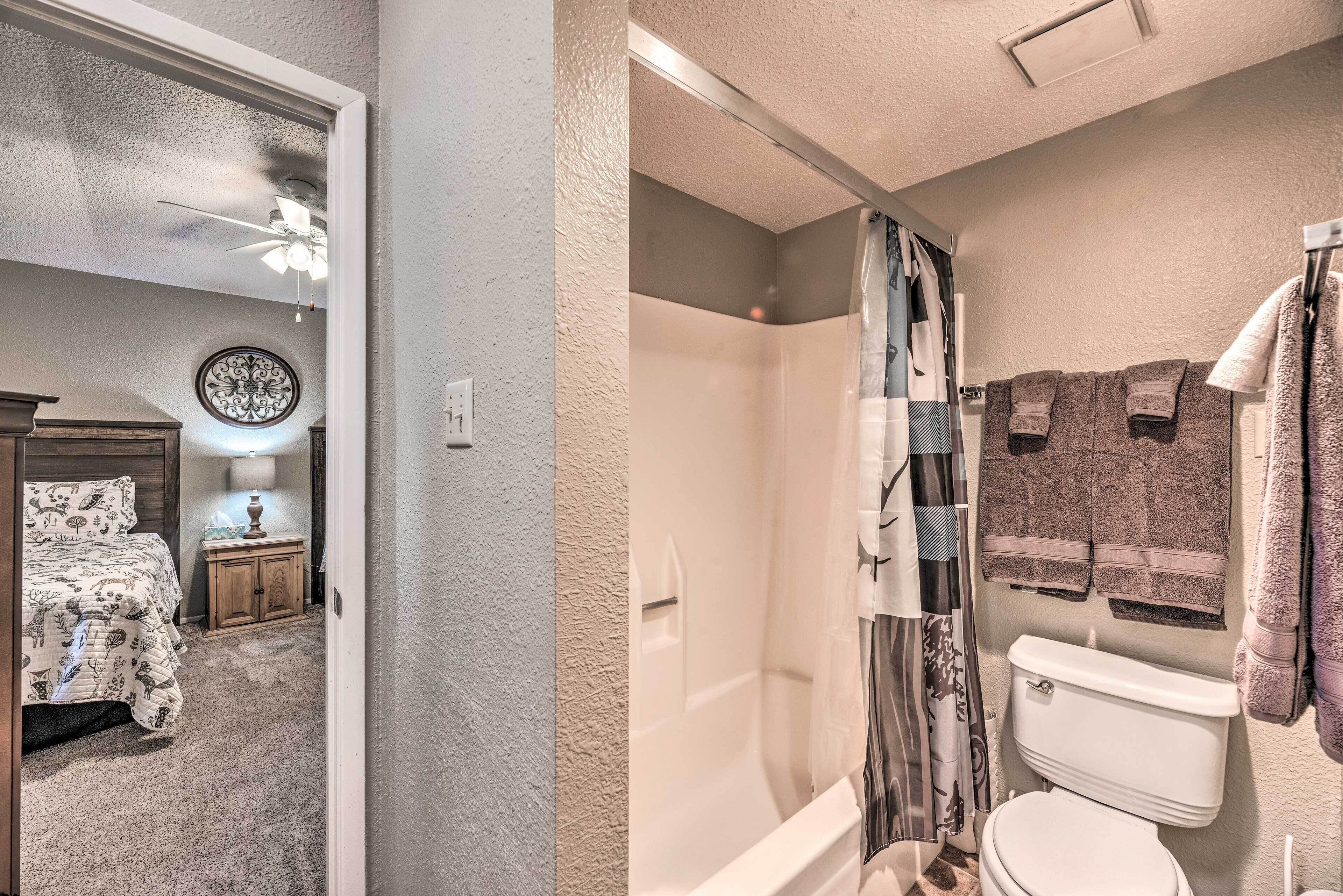 Une chambre à coucher avec un lit, une table de chevet, une lampe et une horloge murale. La salle de bain est équipée d’une douche, de toilettes et de serviettes accrochées au mur.