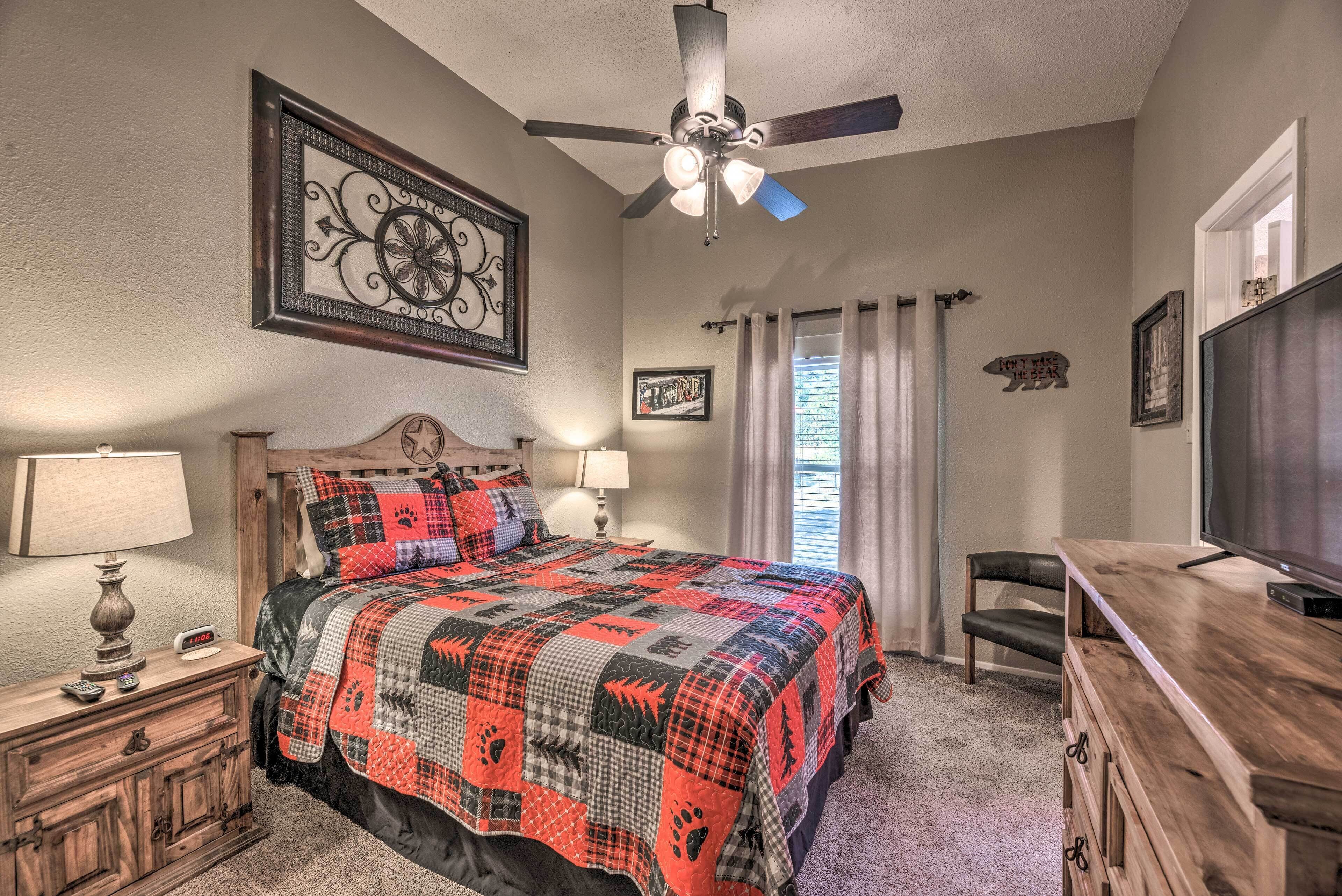 A bedroom with a bed, a ceiling fan, a TV, a dresser, and a nightstand with a lamp.