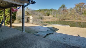 A covered patio with an American flag, a concrete pathway leading to a pond, and a forested area in the background. - Lake Balboa Access: Home w/ Dock & Yard (Hot Springs Village)