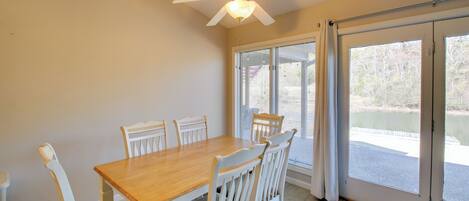 A dining area with a wooden table and white chairs, a ceiling fan, and a sliding glass door leading to an outdoor area.