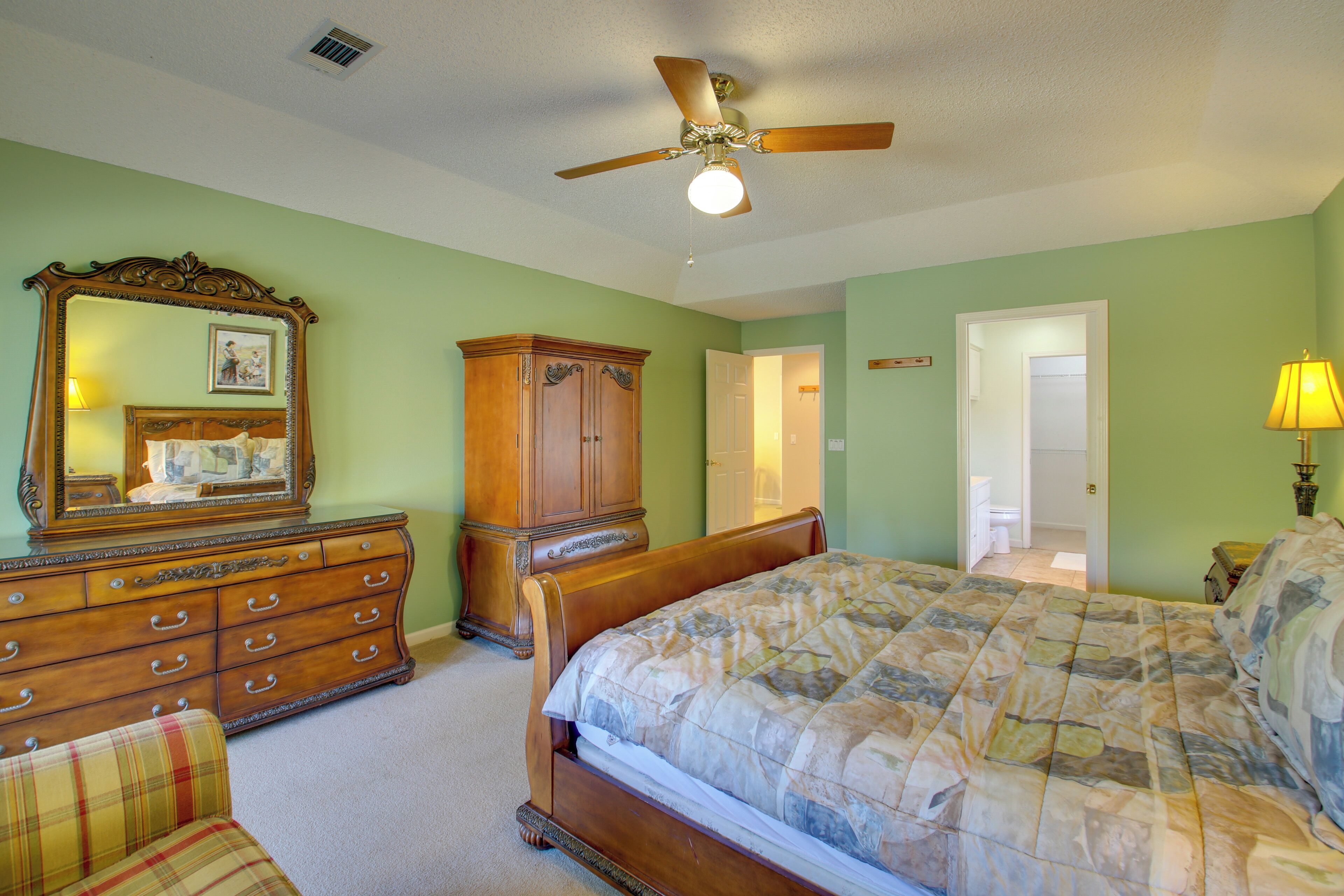 A bedroom with a wooden bed, a dresser, a mirror, and a ceiling fan.