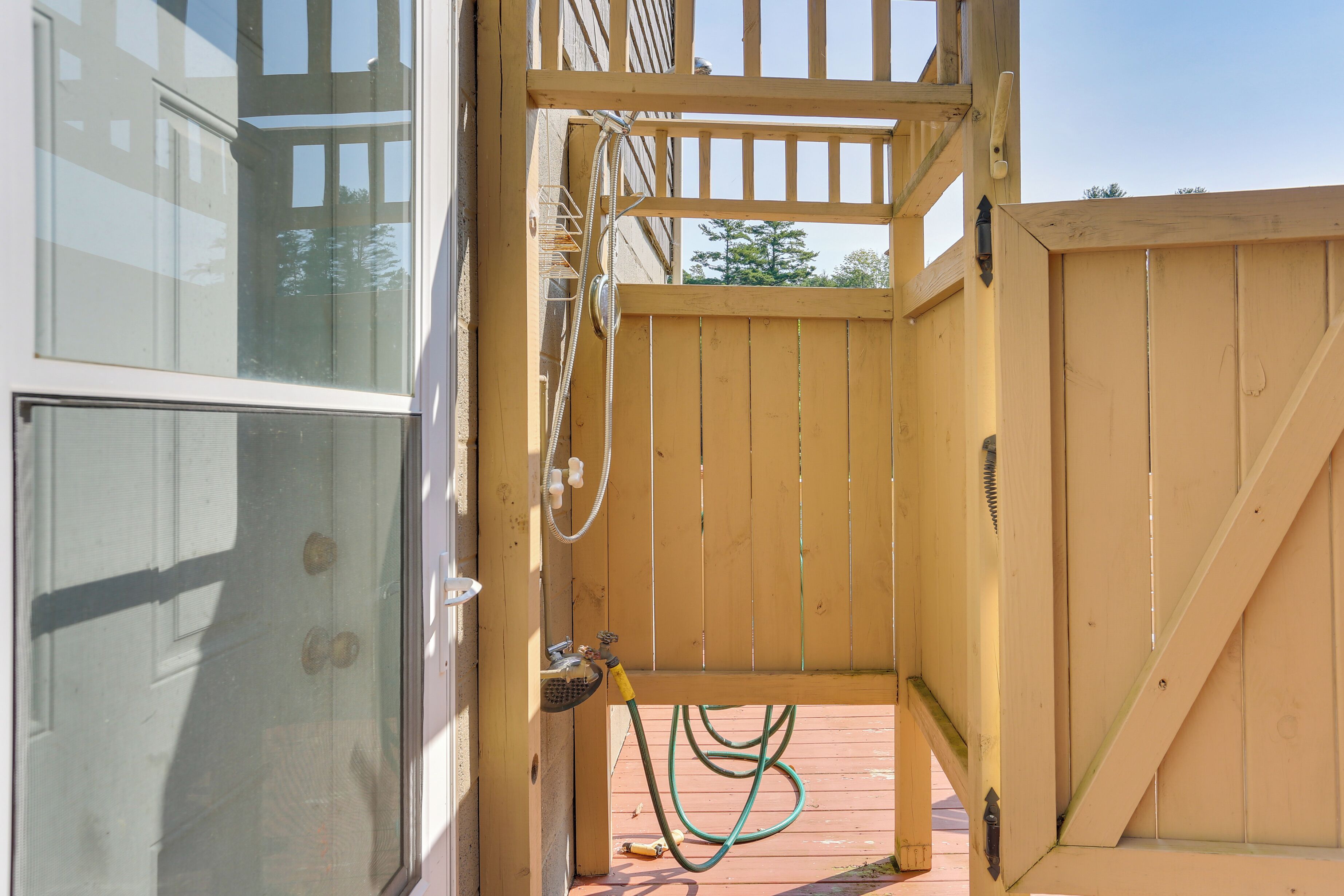 Une porte en bois, avec un tuyau d’arrosage fixé, qui donne sur une terrasse en bois.
