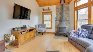 A cozy living room with a fireplace, a comfortable sofa, and a television mounted on the wall. - Pet-friendly Hancock Home on the Delaware River! (Hancock)