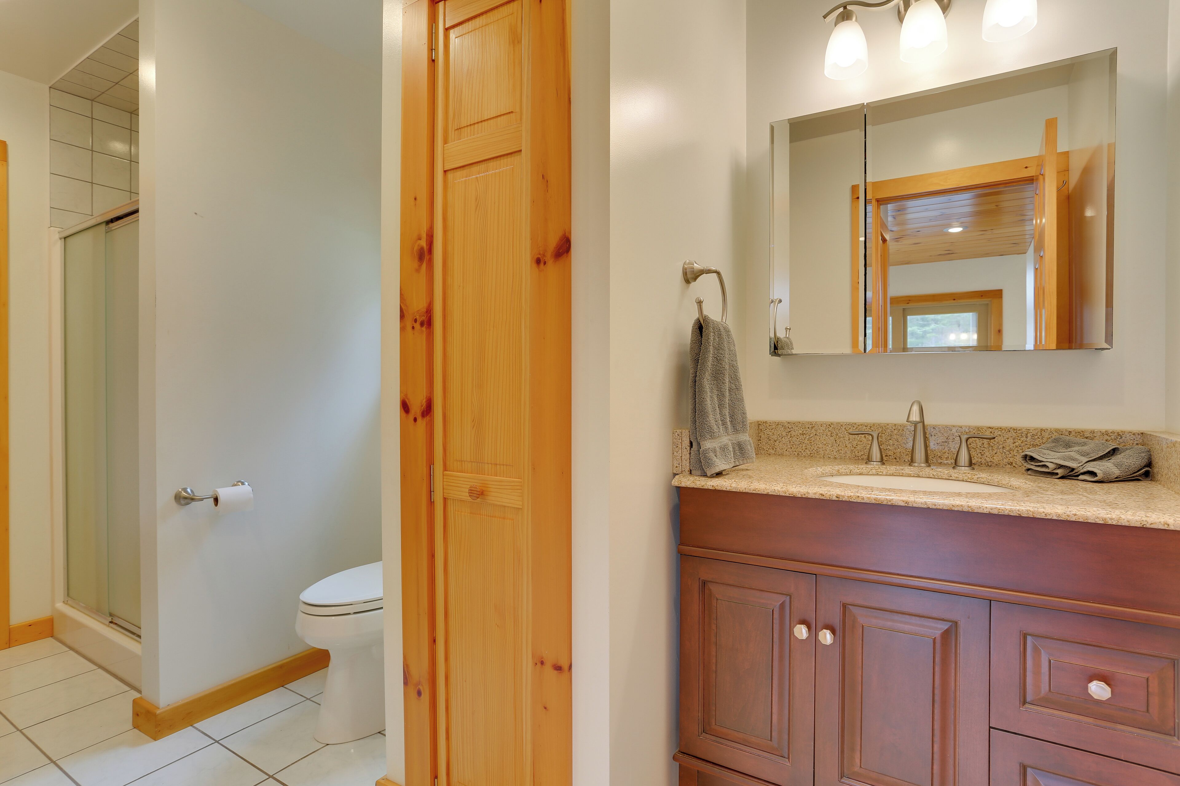 A bathroom with a wooden door, a toilet, a sink with a mirror, and a towel hanging on the wall.