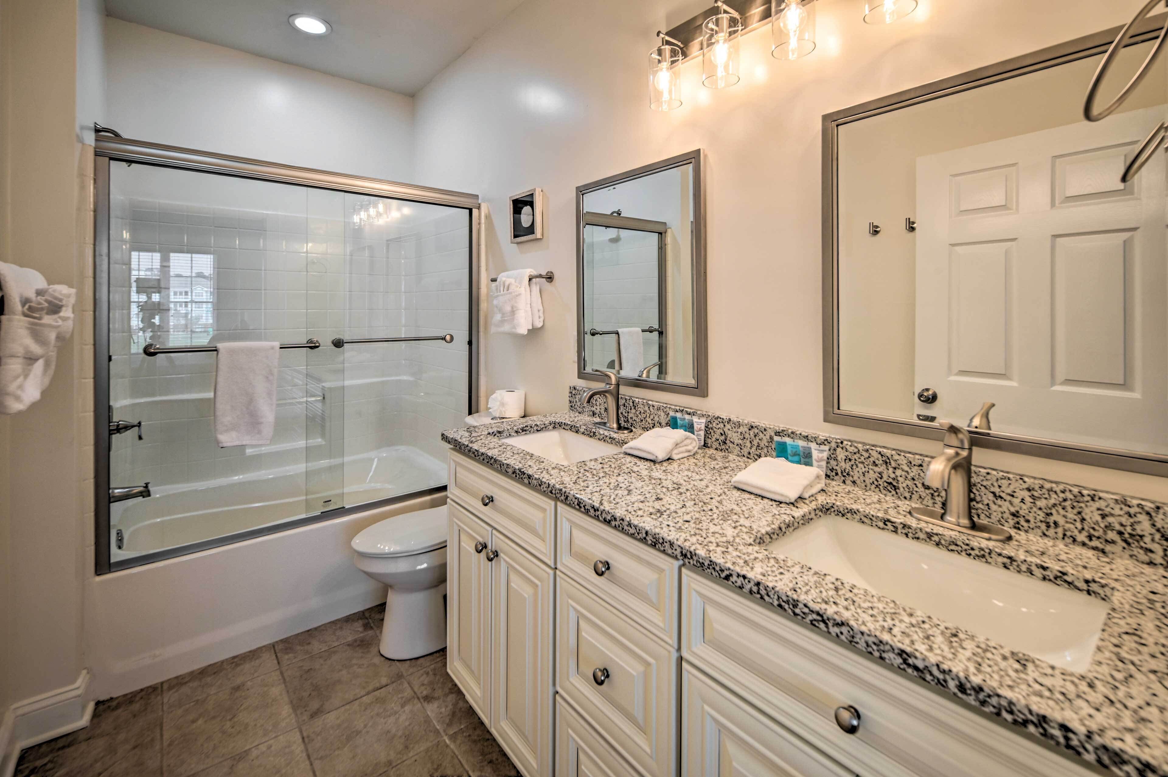 Une salle de bain moderne dot ée d’une douche à parois de verre, de toilettes blanches, d’un lavabo avec un plan de travail en granit et d’un grand miroir au-dessus du lavabo.