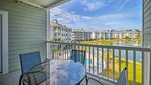 Un balcon avec une table et des chaises en verre, donnant sur une piscine et une rangée de maisons de ville.
