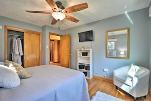 A bedroom with a bed, a ceiling fan, a TV, a wardrobe, and a chair.