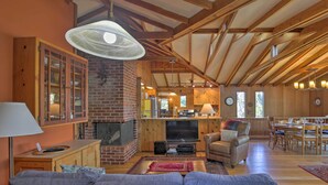 A spacious living room with a fireplace, wooden beams, a television, and a dining area with chairs and a table. - Hillside Home w/ Deck & Views of Tomales Bay! (Inverness)