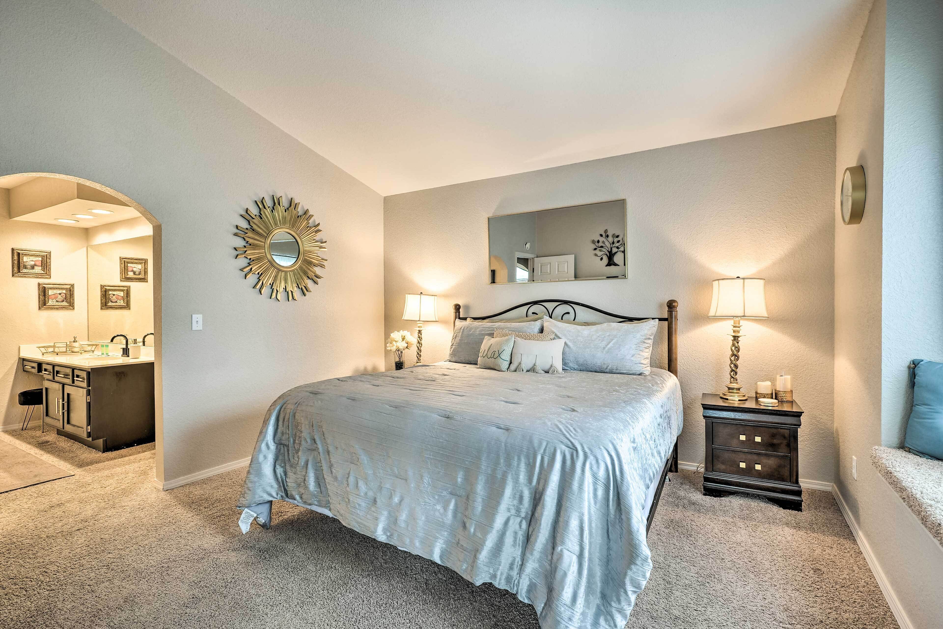 A bedroom with a large bed, bedside lamps, a vanity with a mirror, and a decorative sunburst mirror on the wall.