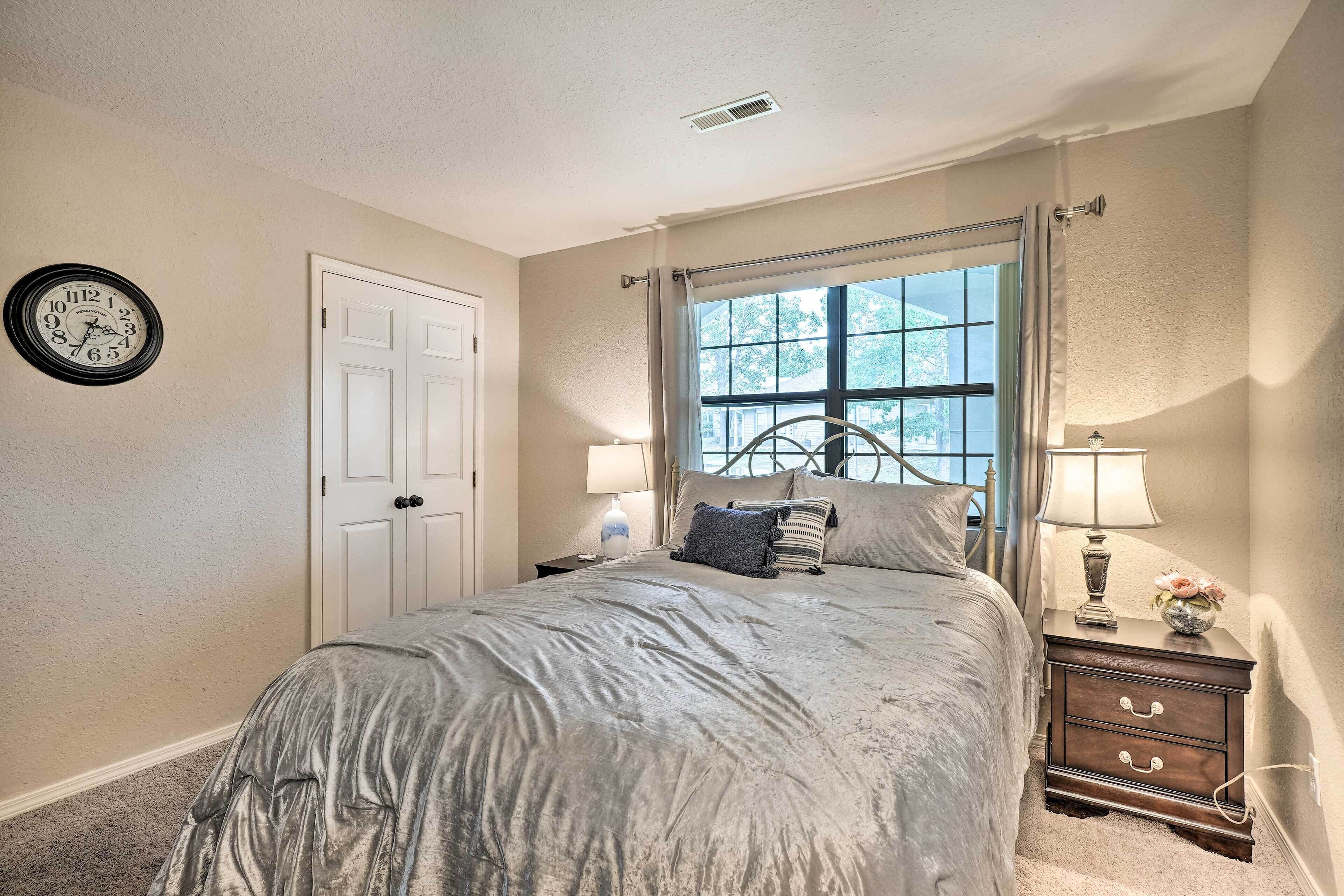 A bedroom with a bed, a nightstand, a lamp, a clock, and a window with curtains.
