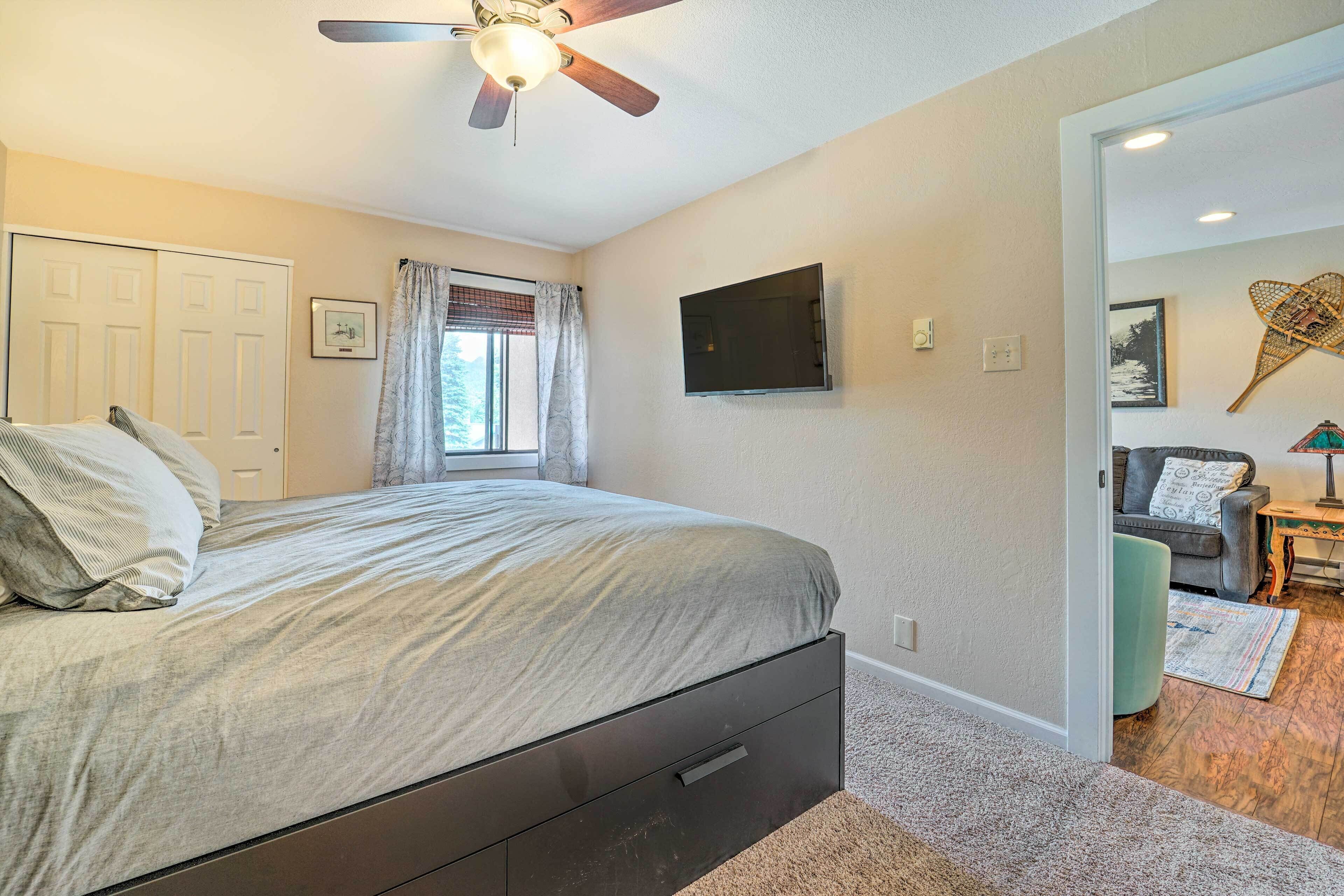 A bedroom with a bed, a ceiling fan, a TV, and a door leading to another room.