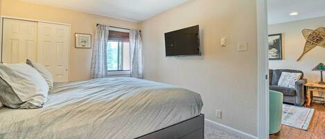A bedroom with a bed, a ceiling fan, a TV, and a door leading to another room.