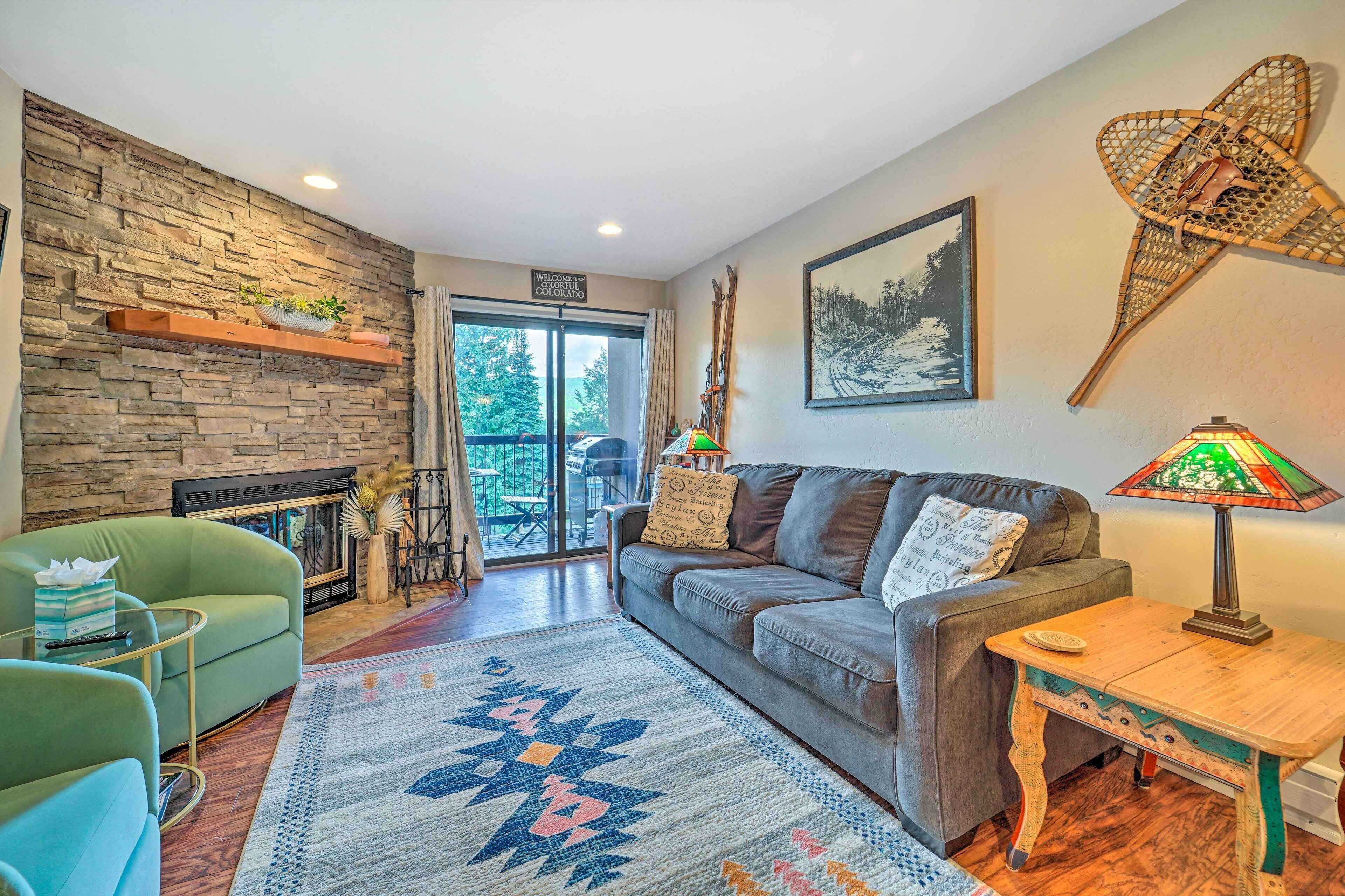 A cozy living room with a stone fireplace, a green armchair, a grey sofa, and a wooden coffee table.