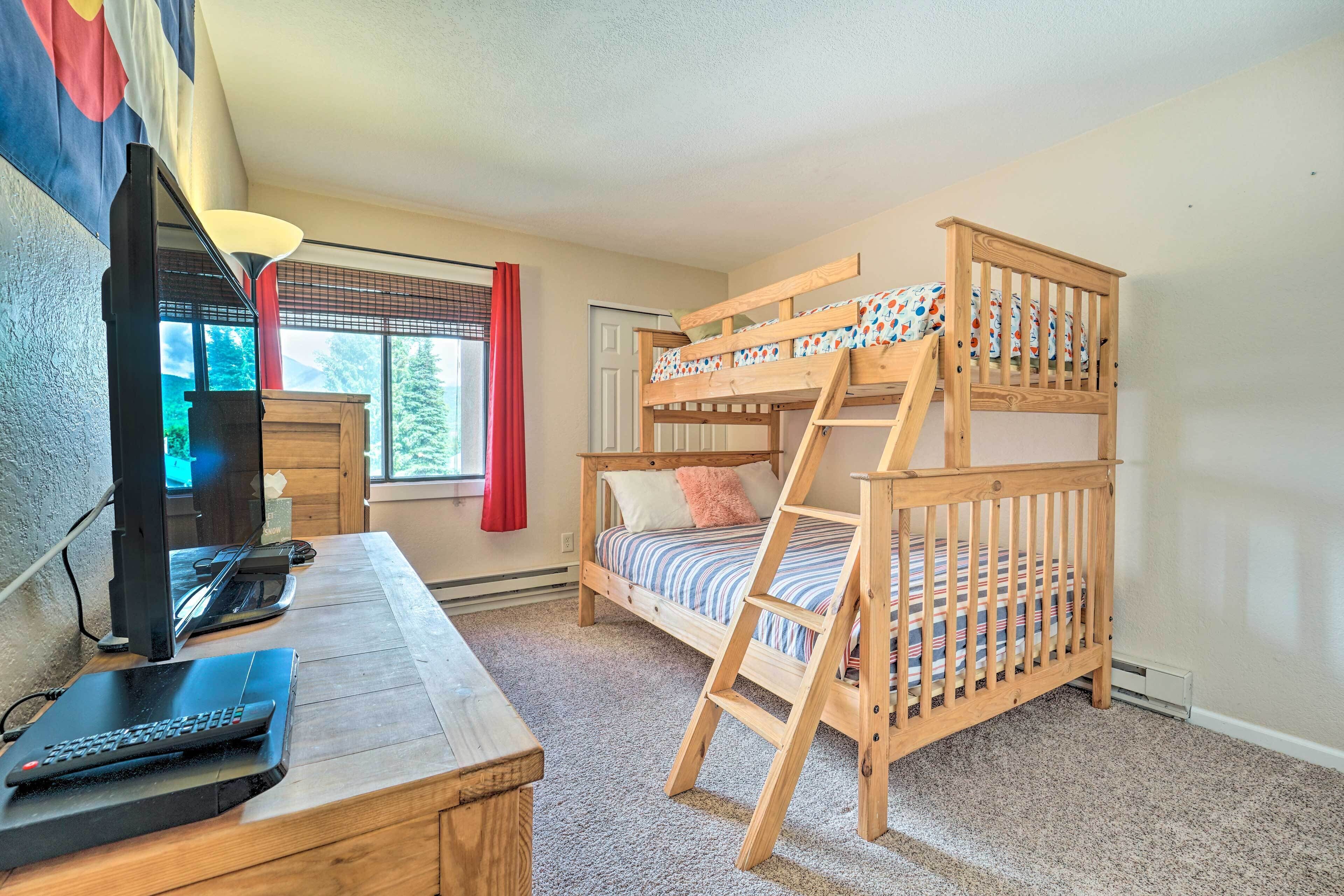A bunk bed with a ladder, a desk with a computer, a television, and a window with curtains.