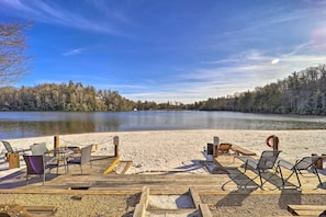 A wooden deck with chairs and tables overlooking a calm lake, surrounded by trees. - Mountain Getaway Home in a Resort Community! (Newland)