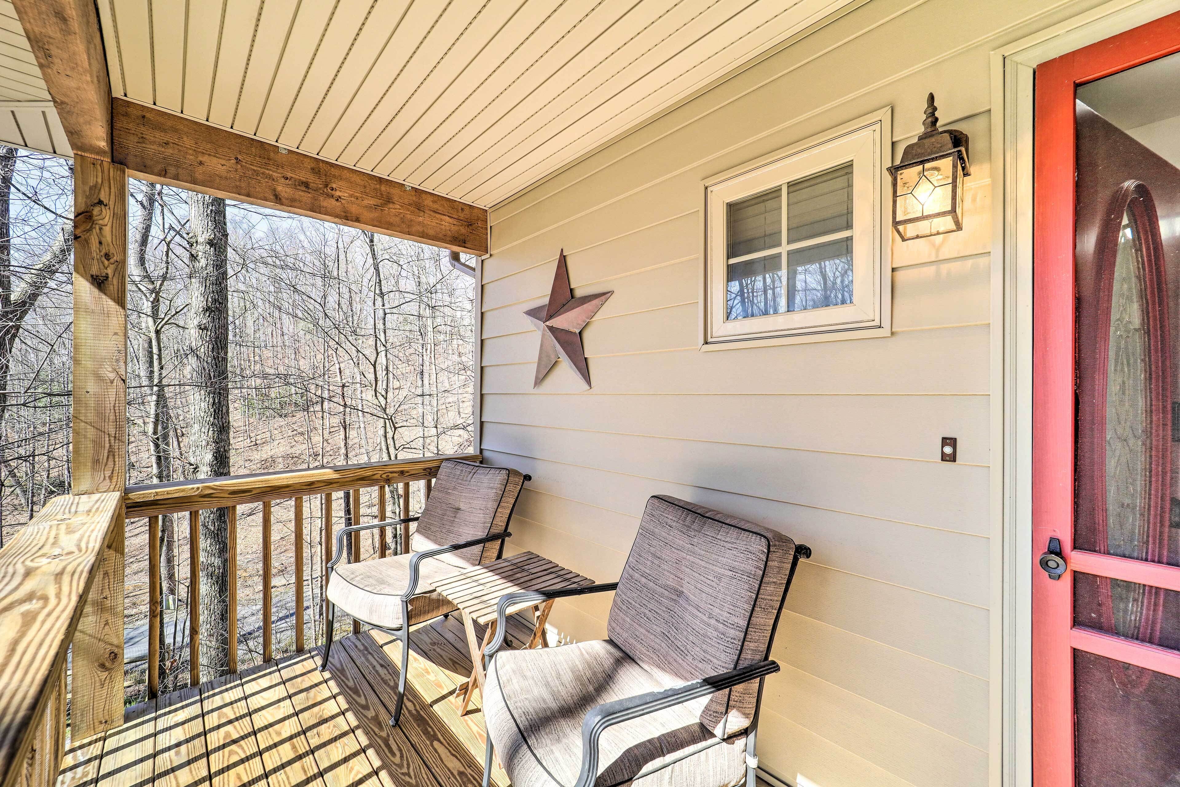 A covered porch with wooden railings, two chairs, a table, a star decoration, a window, and a door.