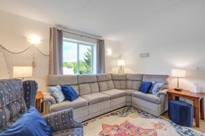 A living room with a sectional sofa, a patterned armchair, a small table with a lamp, and a decorative rug.