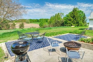 An outdoor patio with a grill, chairs, and a patterned rug.