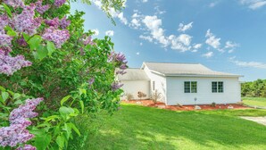 A white single-story house with a well-maintained lawn and a flowering tree in the foreground. - 3 Mi to Lake Michigan: The Country Cottage (Central Lake)