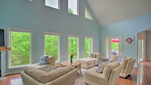 A spacious living room with multiple seating areas, large windows, and a high ceiling.