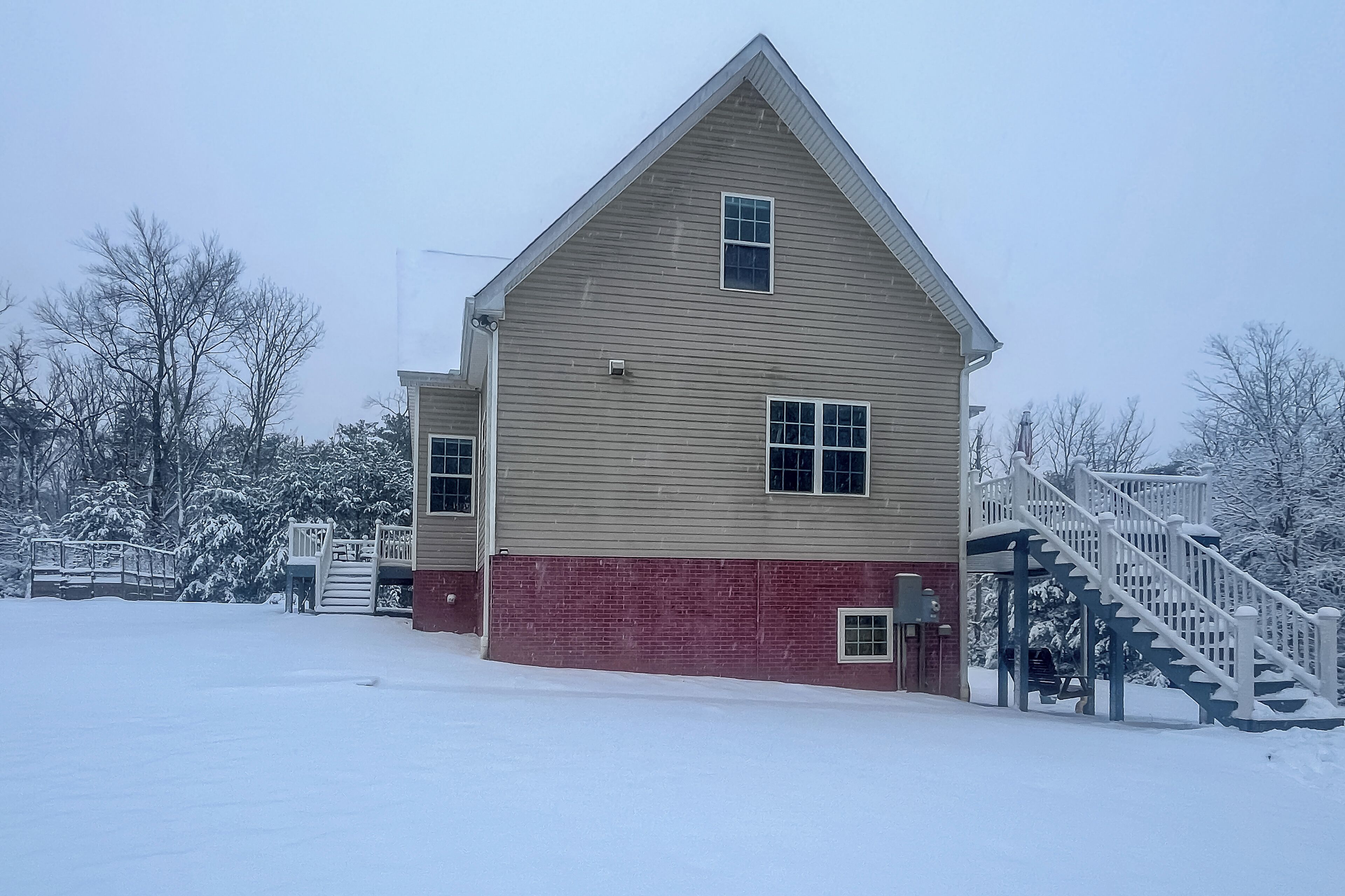 A two-story building with a red brick base and beige siding, featuring a white staircase and a small porch area.