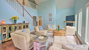 A spacious living room with a high ceiling, a staircase, and a fireplace.