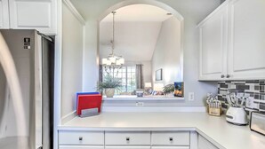 A modern kitchen with white cabinetry, a stainless steel refrigerator, a built-in island with a blender, and a large window providing natural light. - Shuttle to Ocean! North Myrtle Beach Retreat (North Myrtle Beach)